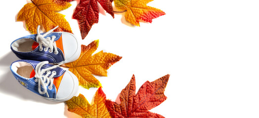 Autumn composition. Frame made of autumn maple leaves on a white background. Children's sneakers. Flat sunbed, top view, space for text.