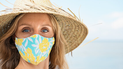 Funny portrait of young woman in straw hat on tropical sea beach. New rules to wear cloth face...