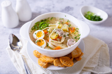 Soup with chicken, noodles, potatoes, quail eggs and carrots. Seasoned with onions and parsley. Close-up.