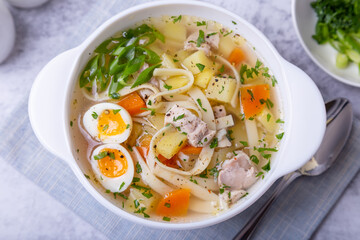 Soup with chicken, noodles, potatoes, quail eggs and carrots. Seasoned with onions and parsley. Close-up.