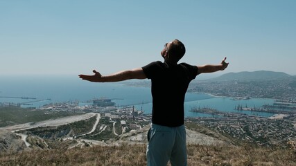Man on the top om hill and spread his arms in different directions. Young bearded man in black t-shirt and sunglasses enjoy the moment.