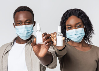 Young couple in face masks showing antiseptic