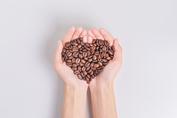 Coffee beans roasted in the hands of woman in heart shape. on white background. Top view.