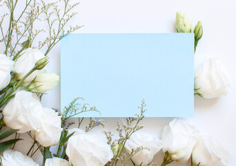 White flowers and light blue rectangular paper on a white top view