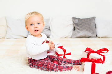 Cute baby with gift box and red christmas ball on white bed background. Christmas congratulations concept with copy space.