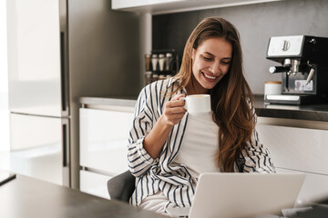 Young caucasian woman working on laptop and drinking coffee at home