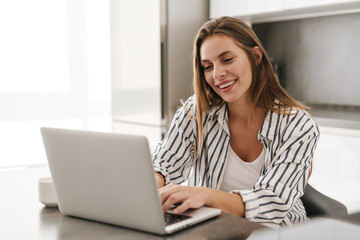Fototapeta na wymiar Young caucasian woman smiling while working on laptop at home