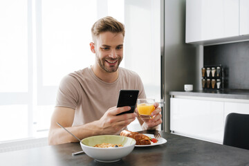 Fototapeta na wymiar Young caucasian man holding cellphone while having breakfast at home