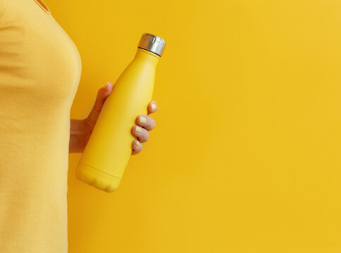 Close up of woman holding yellow reusable bottle on yellow background