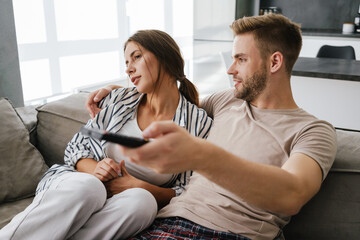 Young couple sitting on sofa and holding remote control at home