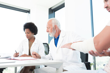 Doctor studying arm injury of patient & assistant writing notes