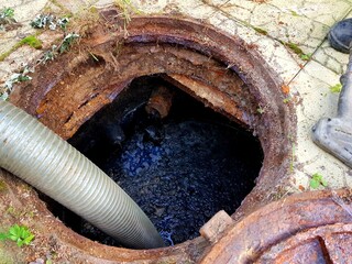 A hose is lowered into the sewer manhole to pump water out of the pit