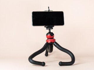 A desktop tripod with a smartphone attached to it stands on a light background. Ease of communication. Tripod with flexible legs.