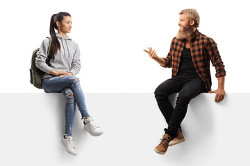 Bearded guy sitting on a white panel and talking to a female student