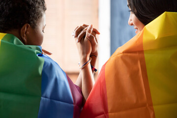Black African LGBT woman covering LGBTQ rainbow flag with asian LGBT woman upside down, gay pride...