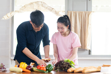 Asian young couples are cutting vegetables and smiling while cooking in kitchen at home