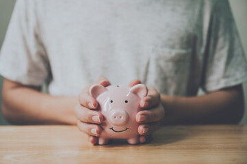 Man hand holding piggy bank on wood table. Save money and financial investment