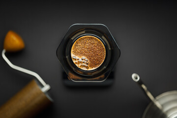 Aeropress coffee maker with scales, coffee grinder and kettle on a black background top view. Aeropress with coffee in focus, background blurred.