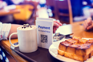 Selective focus to QR code payment tag with blur bread set meal and coffee in coffee shop or restaurant to accepted generate digital pay without money. Qr code payment concept.