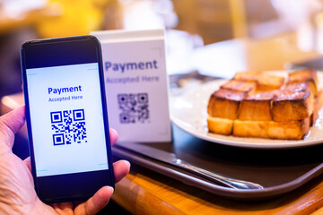 Naklejka na ściany i meble Customer hand using smart phone to scan QR code tag with blur bread set meal in coffee shop or restaurant to accepted generate digital pay without money. Qr code payment concept.