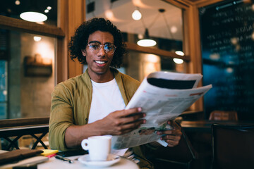 Cheerful man with newspaper sitting at table in cafe