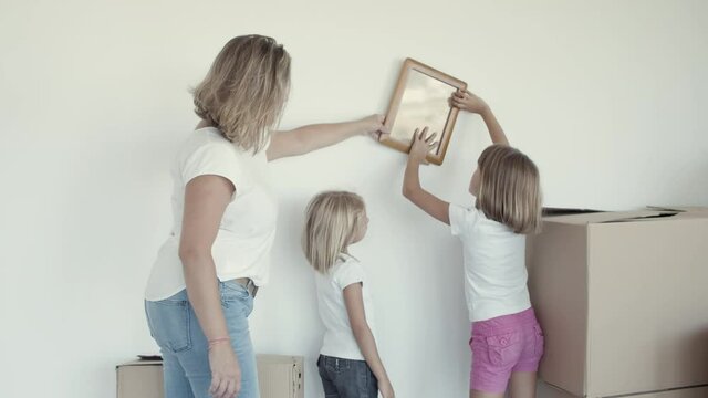 Two girls and their mom choosing place on wall for picture frame. Family establishing new home together. Moving into new apartment concept