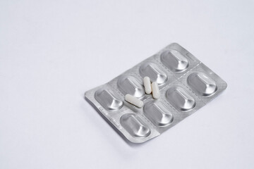 Three white pills capsule lie on medicine in silver aluminium blister pack on white table. Isolated. Copy space. Top view. Concept pharmacy, medicine, healthcare, painkillers, drug, abuse