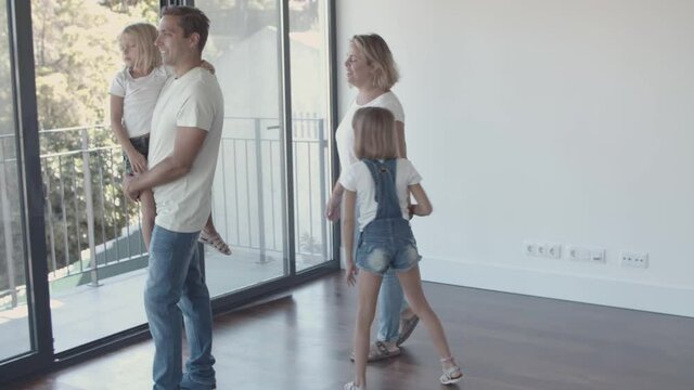 Happy family with two kids looking over their new apartment. Dad holding and carrying girl in arms. New home concept