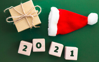 Holiday present, santa hat and wood cubes with text 2021 on dark green background. Happy New Year and Merry Christmas concept.