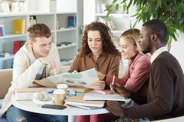 Multi-ethnic group of young people studying together while sitting at table in college library and working on group project