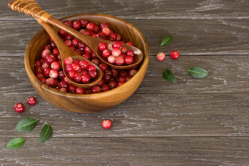 ripe cranberries in a wooden bowl and spoons on the table. background with cranberries and a copy of the space. cranberries in a bowl close-up.