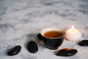 Obraz na płótnie Canvas Tea cup, black spa stones, candle on gray concrete background. Wellness concept. Top view, flat lay, copy space