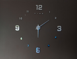 Clock on dark wall texture. The 12th numbers of time and letter T I M E are silver color. Clockwise is pointing to number six, shown at 6 O'clock or 6 p.m. approximately.
