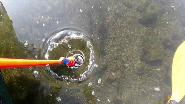 top view of Dropping a magnet for magnet fishing in slow motion into a river and watching the splash and bubbles as the fisher searches for treasures on the river bead.