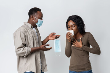 Black man in mask holding another mask for coughing woman