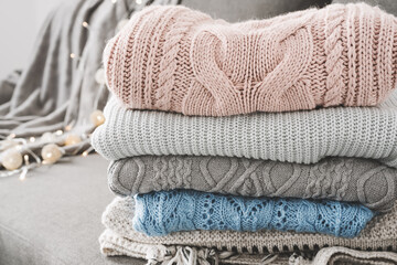 Neat and tidy pile of warm sweaters on gray sofa. Knitwear care. Knitted jumpers for cold fall and winter season