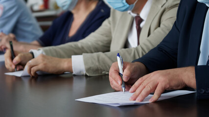 A group of businessmen or officials signs documents at a business meeting during a pandemic. People in suits and medical masks. Reportage