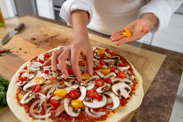 Obraz na płótnie Canvas A close-up of the chef's hands adding yellow tomatoes to the pizza toppings. Vegan food.