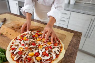 A close-up of the chef's hands adding yellow tomatoes to the pizza toppings. Vegan food.