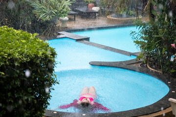 young girl lies in the water of a tropical outdoor pool in the pouring rain