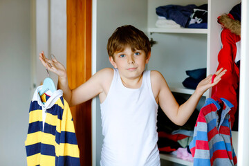 School kid boy standing by wardrobe with clothes. Child making decision for school shirt to wear. Children get dressed in the morning for school.