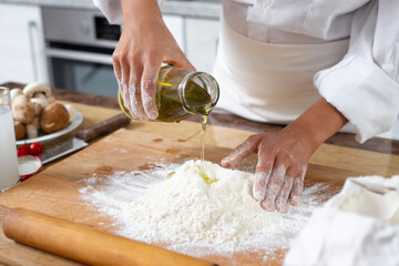 Close-up. The cook pours olive oil from a bottle into a handful of flour on the table.