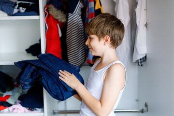 School kid boy standing by wardrobe with clothes. Child making decision for school jeans pants to wear. Children get dressed in the morning for school.