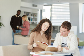 Portrait of two young students boy ad girl studying together while sitting at table in college library and smiling, copy space
