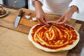 A view of the hands of a chef who is beginning to lay out onions on top of a piece Cooking pizza.