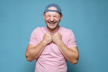 Naklejka premium Caucasian man is very happy and in anticipation of a pleasant surprise. He pressed fists to chest, closed eyes and smiled broadly. 