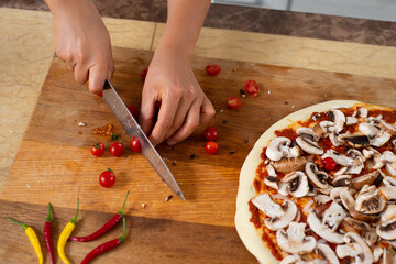 Top view of the hands of a chef chopping with a knife cherry tomatoes on a wooden board. Cooking vegan pizza.