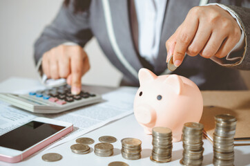 Closeup image businesswoman holding coins putting into piggy bank and calculating. concept saving money wealth for finance accounting.