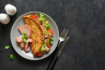 Beautiful breakfast with tomatoes, ham and salad on a black background. Pancake with filling, top view.