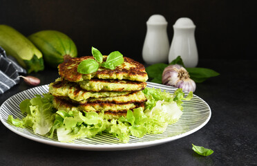 Zucchini pancakes with sauce and garlic on a concrete black background.